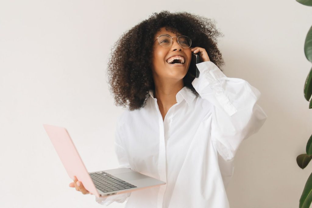 Femme souriante en télétravail, au téléphone avec un ordinateur portable à la main