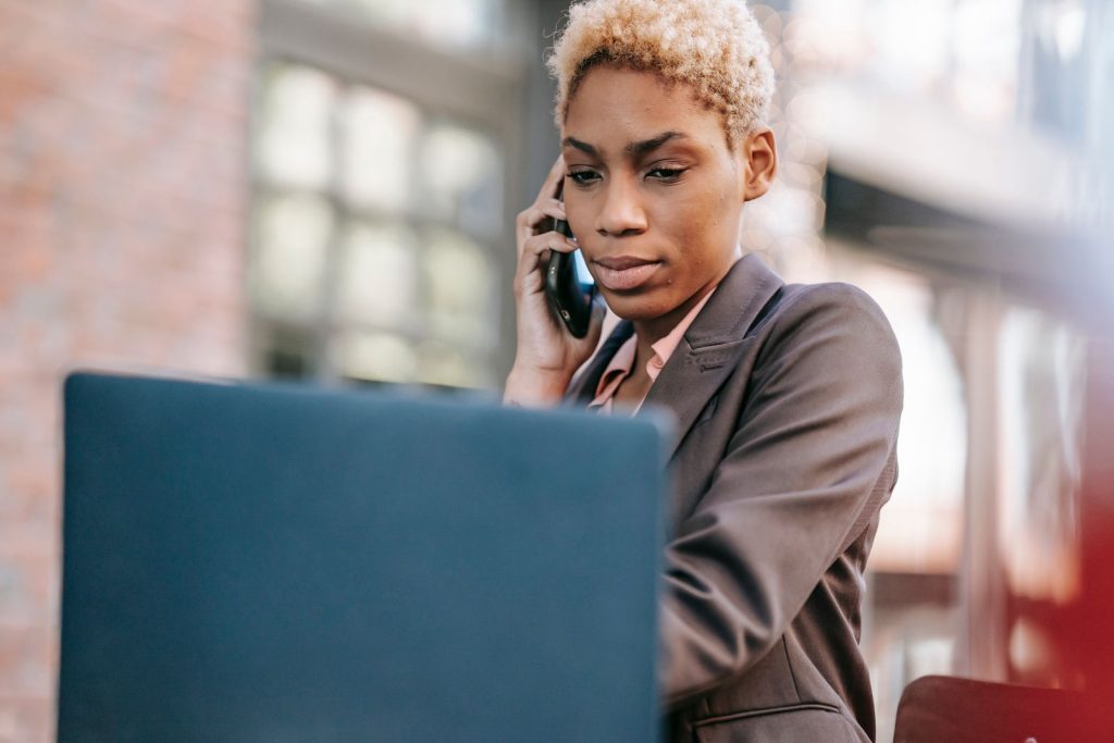 Jeune professionnelle en veste de tailleur au téléphone devant son ordinateur portable, concentrée sur son appel