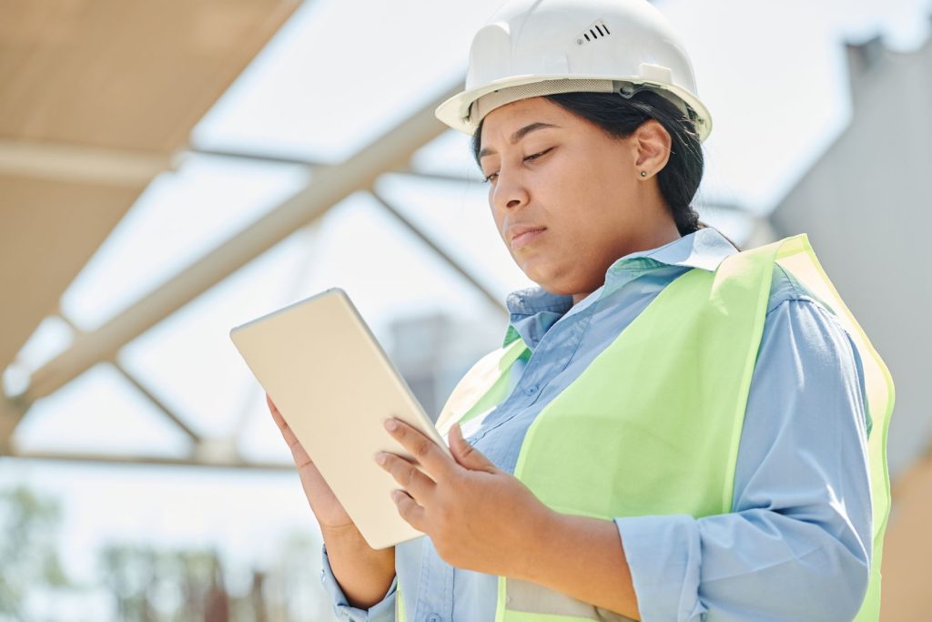 Ingénieure en casque et gilet de sécurité consultant une tablette sur un chantier en extérieur