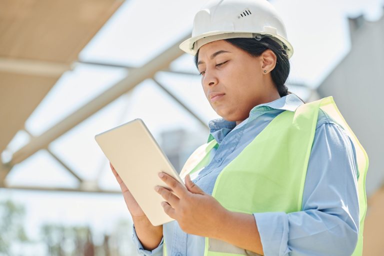 Ingénieure en casque et gilet de sécurité consultant une tablette sur un chantier en extérieur